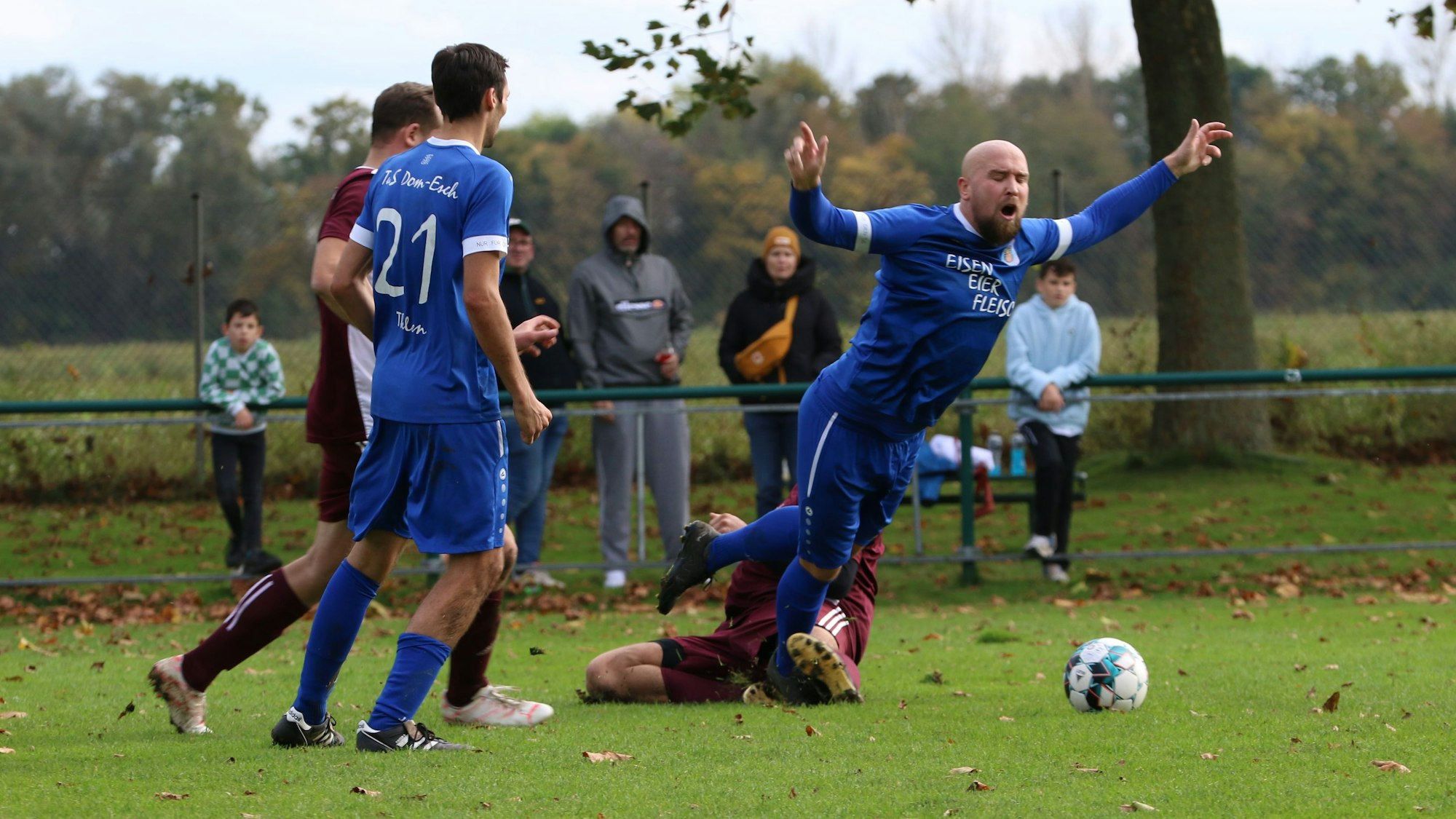 Ein Fußballspieler fällt nach einer Grätsche des Gegenspielers mit ausgestreckten Armen zu Boden.