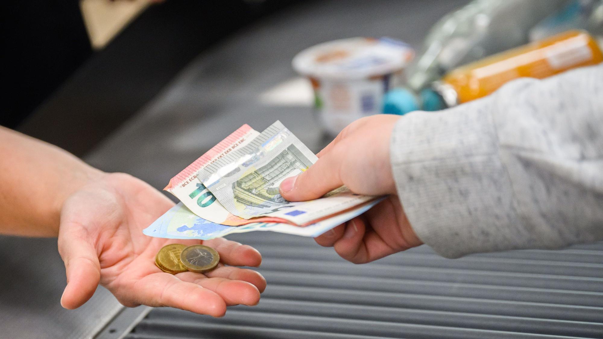 Eine Kassiererin gibt einer Kundin Wechselgeld an der Kasse eines Supermarktes.