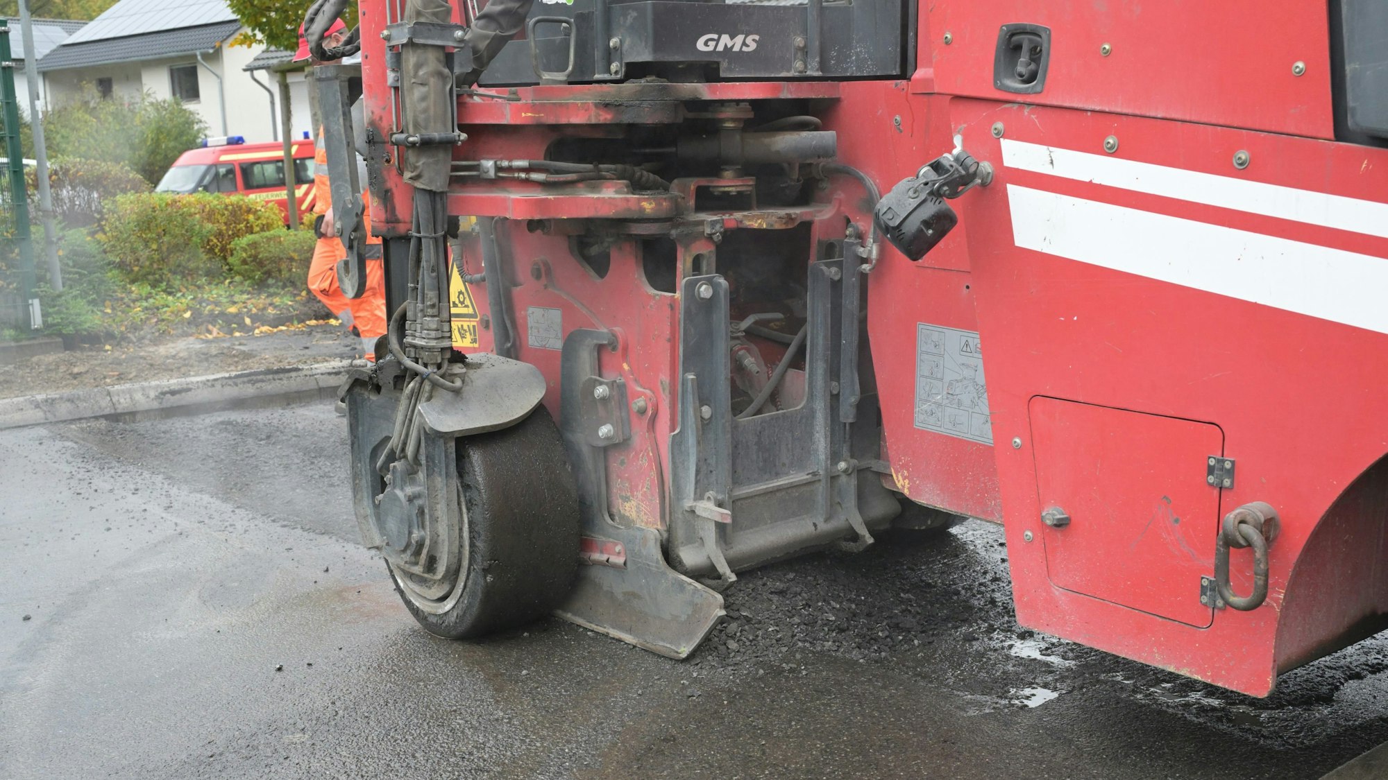 Eine rote Fräsmaschine entfernt den Asphalt einer Straße.