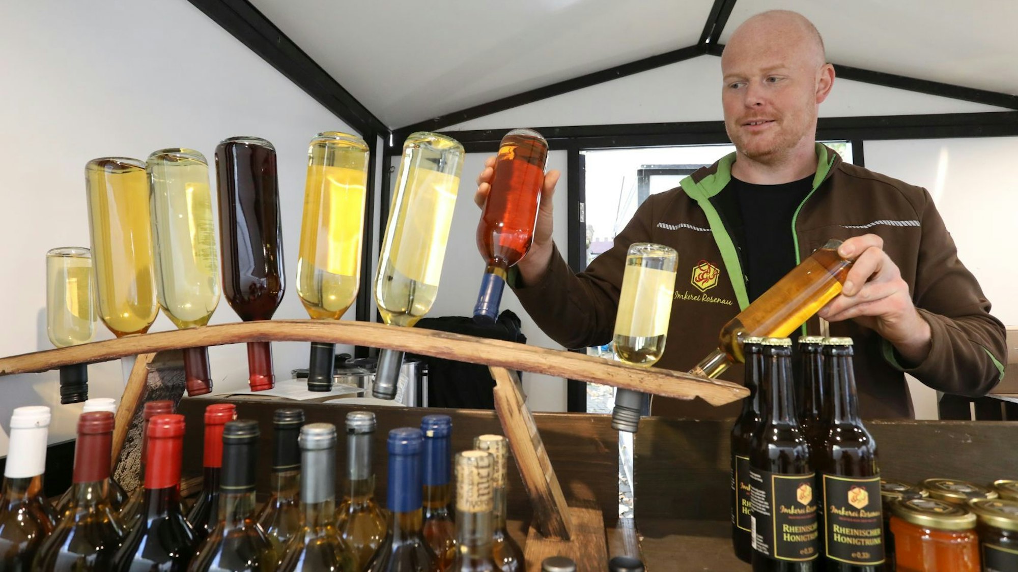 Mehrere Flaschen an einem Marktstand, ein Mann hält zwei in den Händen.