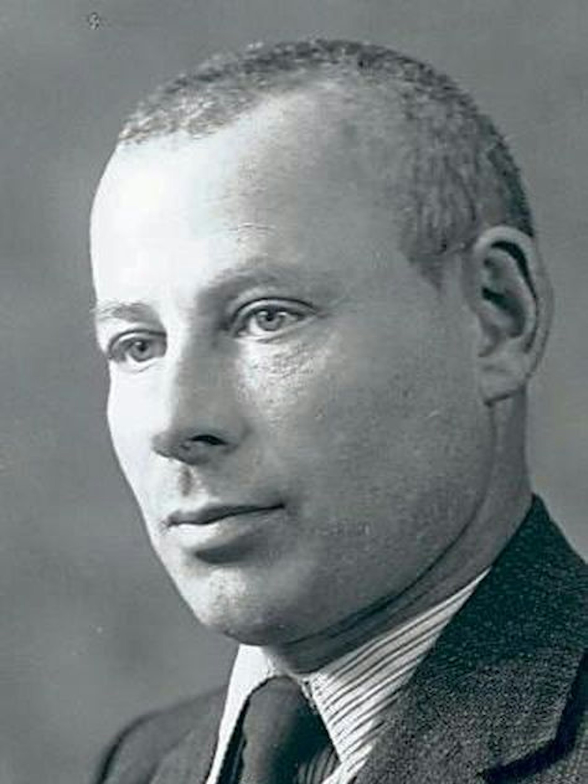 Schwarz-Weiß-Bild eines ernst schauenden Mannes im Anzug, Hemd und Krawatte.