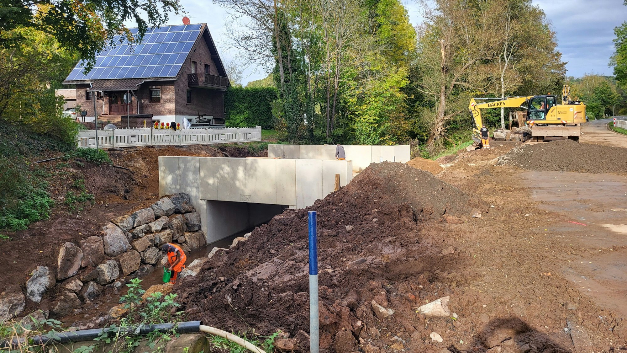Das Bild zeigt eine neu gebaute Brücke, links ist sie mit Warnbarken abgesperrt, rechts sind Erdhügel und ein Bagger zu sehen.