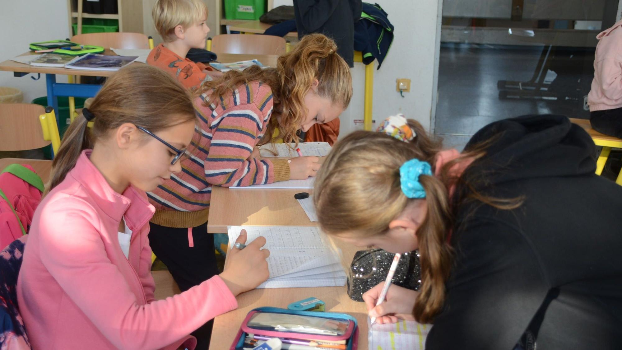 Mädchen sitzen an Schultischen und schreiben in ihre Hefte.