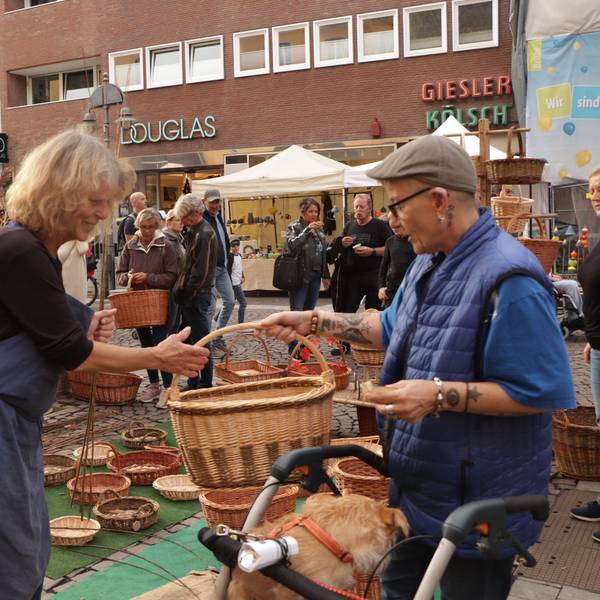Eine Frau an einem Stand mit geflochtenen Körben überreicht jemandem einen Korb.