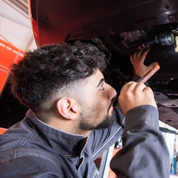 Ein Kfz-Mechaniker begutachtet einen Schaden an einem Auto.