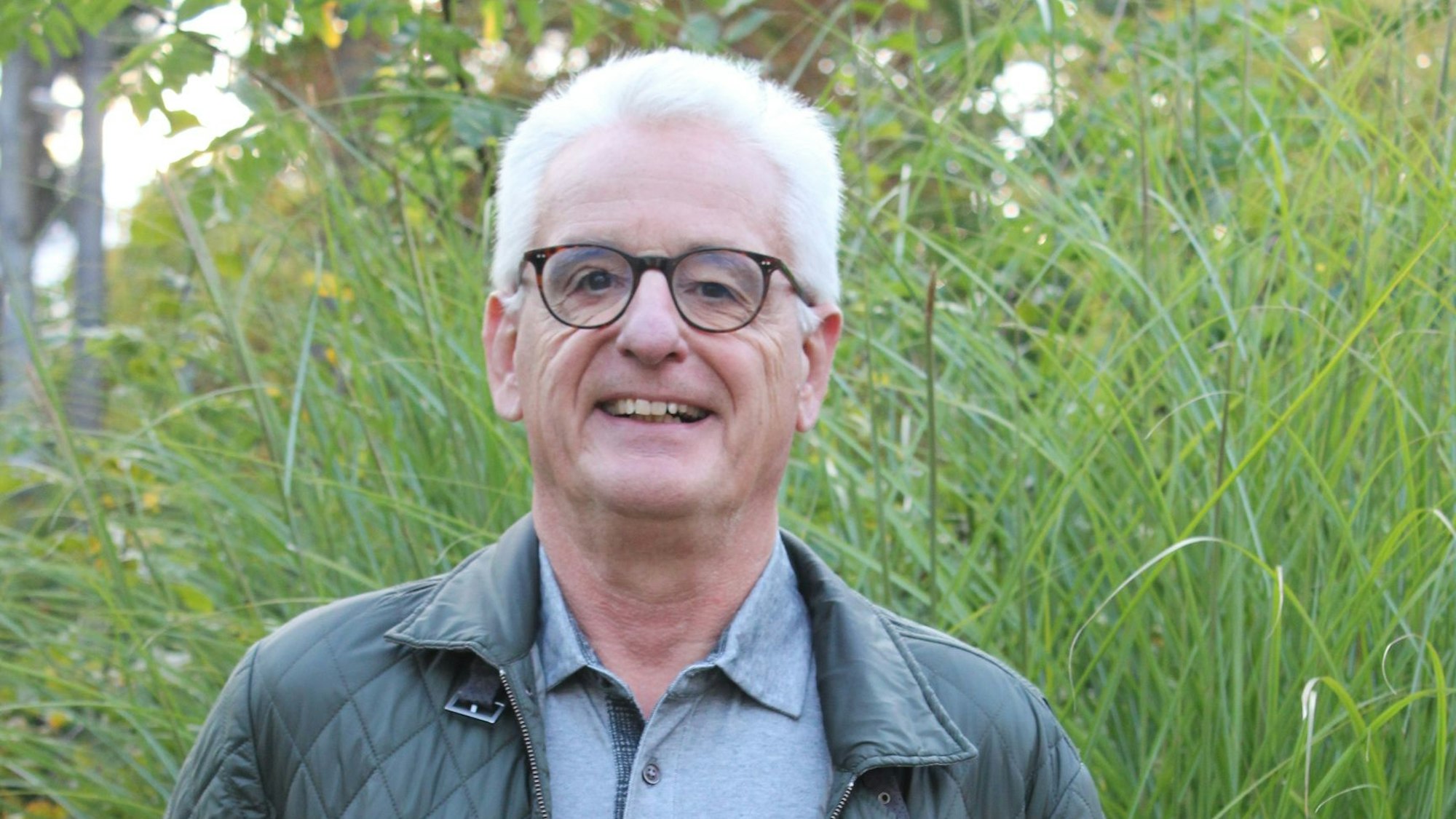Der Autor steht draußen in der freien Natur, hinter ihm wächst hohes Gras.