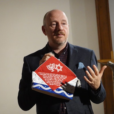 Ein Mann mit einer Kappe in der Hand steht an einem Rednerpult.