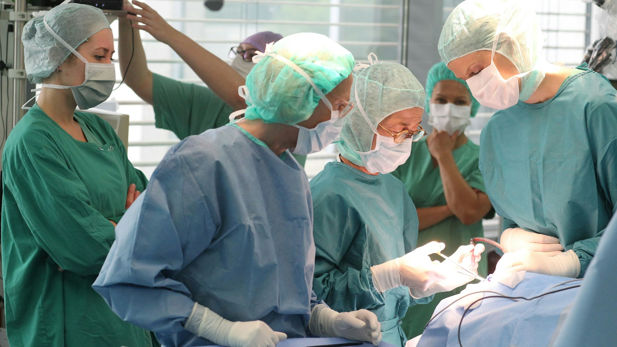 Mehrere Ärzte und Schwestern in Kitteln bei einem chirurgischen Eingriff.
