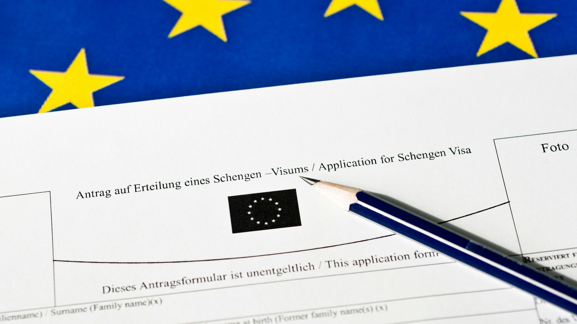 Ein Stift liegt auf einem Antrag auf Erteilung eines Schengen-Visums. Im Hintergrund ist die EU-Fahne zu erkennen.