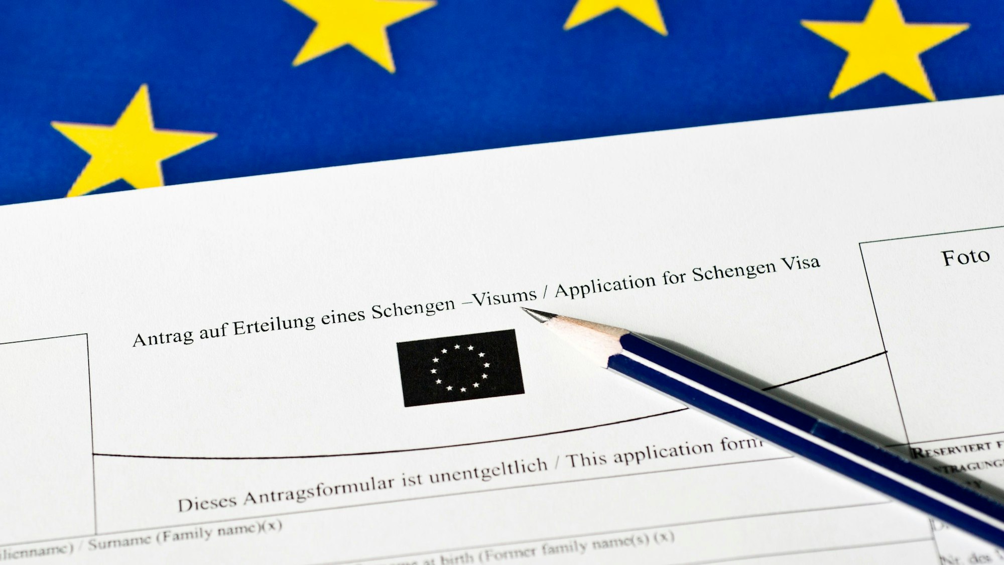 Ein Stift liegt auf einem Antrag auf Erteilung eines Schengen-Visums. Im Hintergrund ist die EU-Fahne zu erkennen.