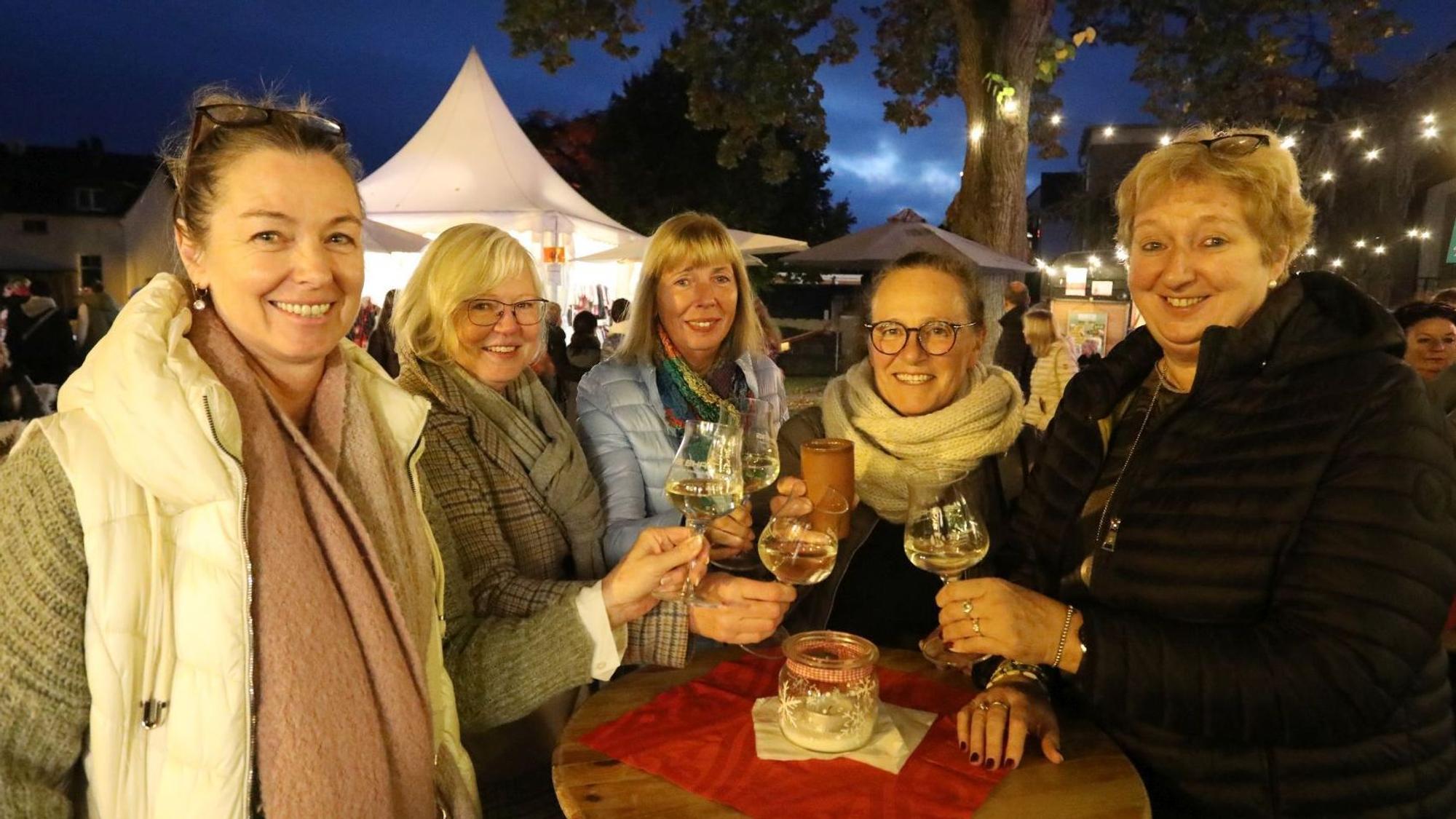 Fünf Frauen stoßen an einem Stehtisch mit ihren Weingläsern an.