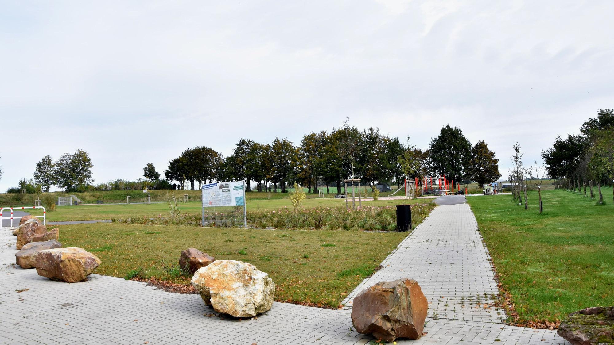 Zu sehen ist ein Rasenplatz mit Weg und Spielplatz in der Ferne, davor stehen große Steine.