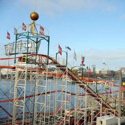 Eine Achterbahn steht am Rheinufer. Im Hintergrund ist der Kölner Dom zu sehen.