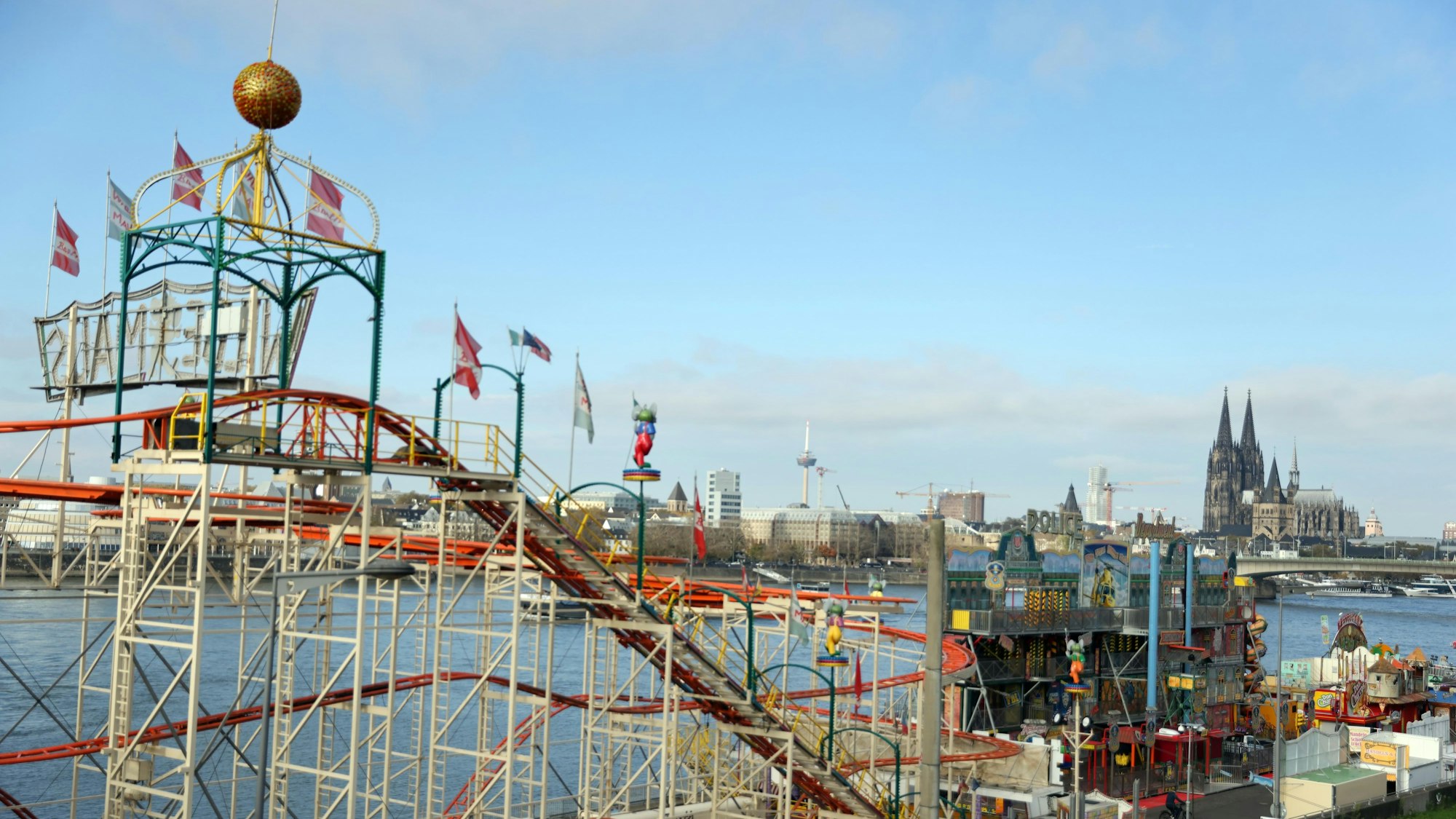 Eine Achterbahn steht am Rheinufer. Im Hintergrund ist der Kölner Dom zu sehen.