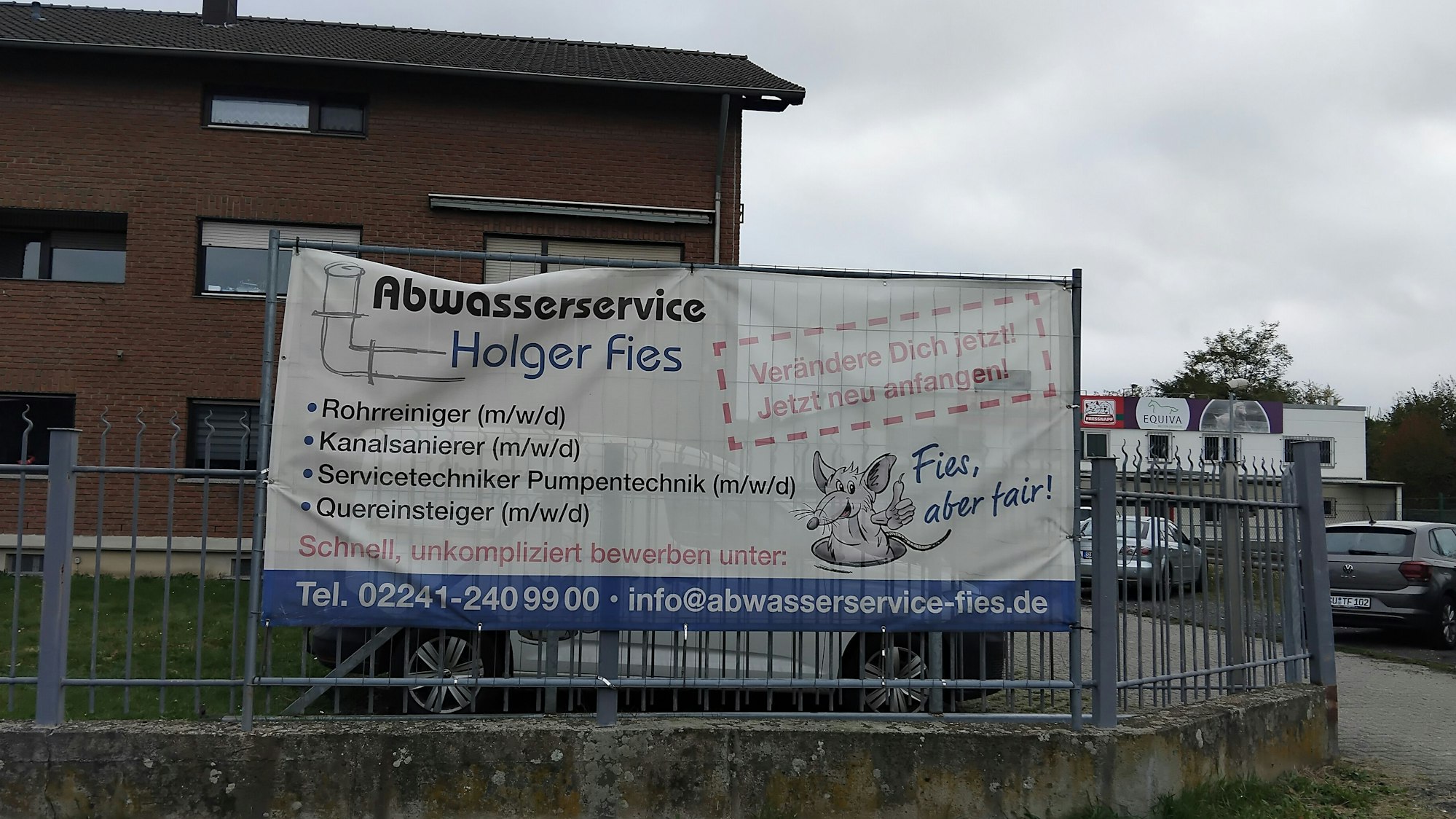 Vor einem Bachsteingebäude ist ein Plakat aufgehängt, auf dem verschiedene Stellenausschreibungen gelistet sind: Rohrreiniger, Kanalsanierer, Servicetechniker Pumpentechnik und Quereinsteiger.