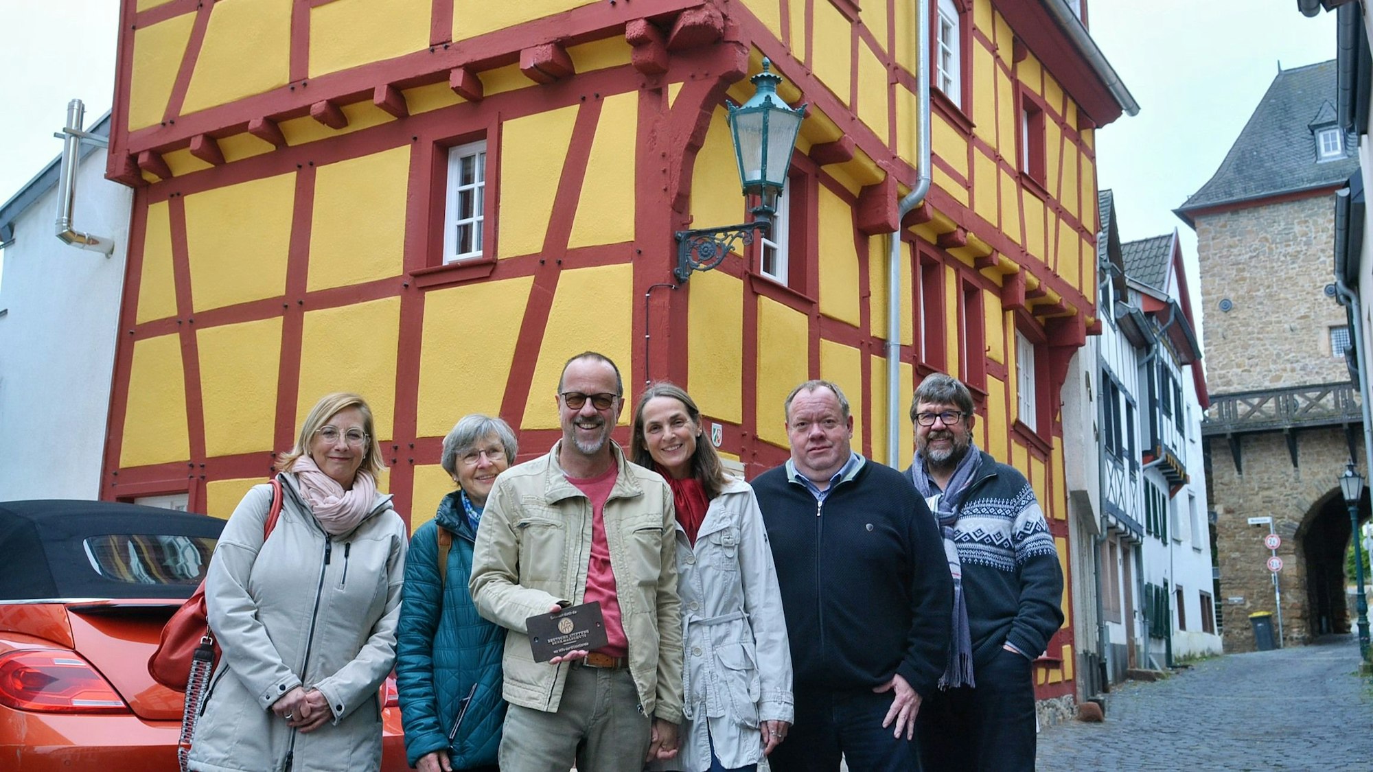 Eine Gruppe Menschen steht vor einem Fachwerkhaus mit gelben Gefachen und roten Balken.