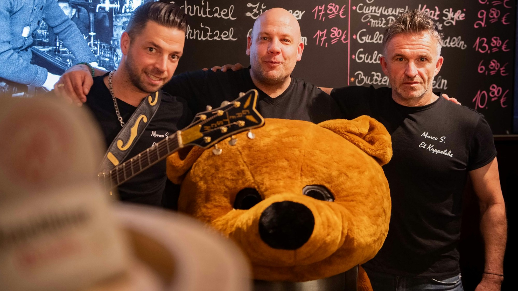 Das Bild zeigt die drei Organisatoren, die sich in den Arm nehmen. Vor Jörg Peter liegt ein überdimensionaler Plüschbärenkopf.