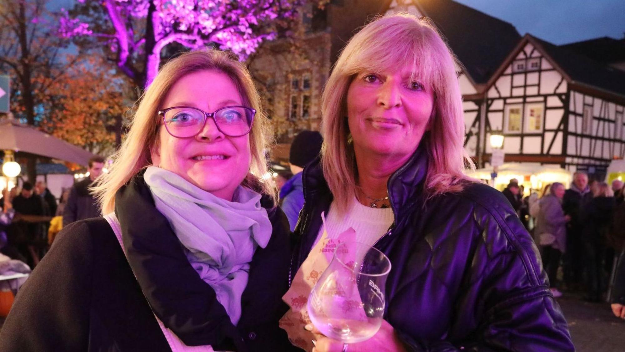 Zwei Frauen auf dem Marktplatz, im Hintergrund ist ein Fachwerkhaus zu sehen.