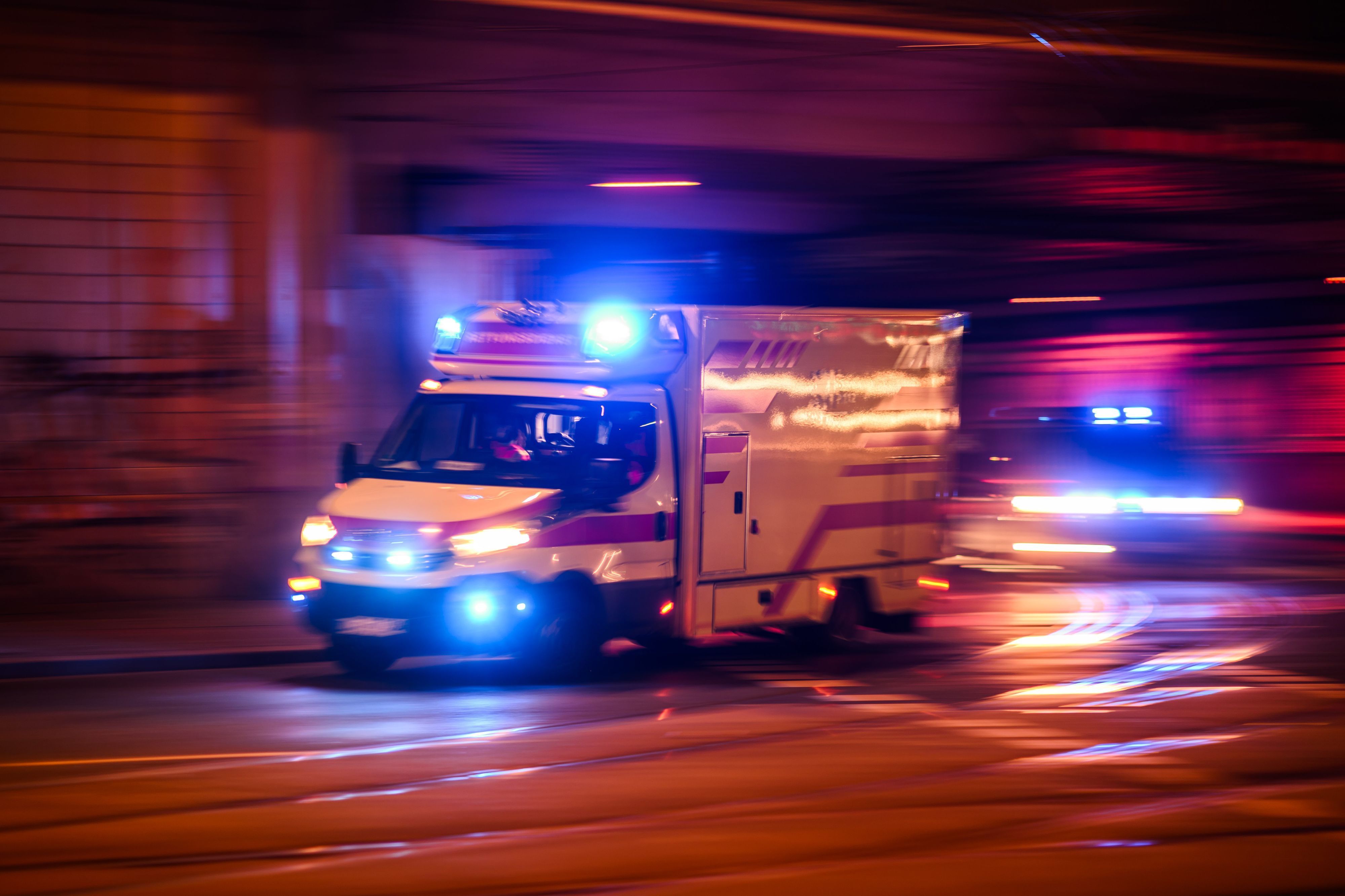 ARCHIV - 30.01.2024, Sachsen, Dresden: Ein Rettungswagen fährt am Abend auf der Antonstraße im Stadtteil Leipziger Vorstadt mit Blaulicht zu einem Einsatz, dahinter fährt ein Polizeiauto. (Aufnahme mit langer Belichtungszeit) (zu dpa: «Polizei: 13-Jährige verletzt Schwester - Siebenjährige tot») Foto: Robert Michael/dpa +++ dpa-Bildfunk +++