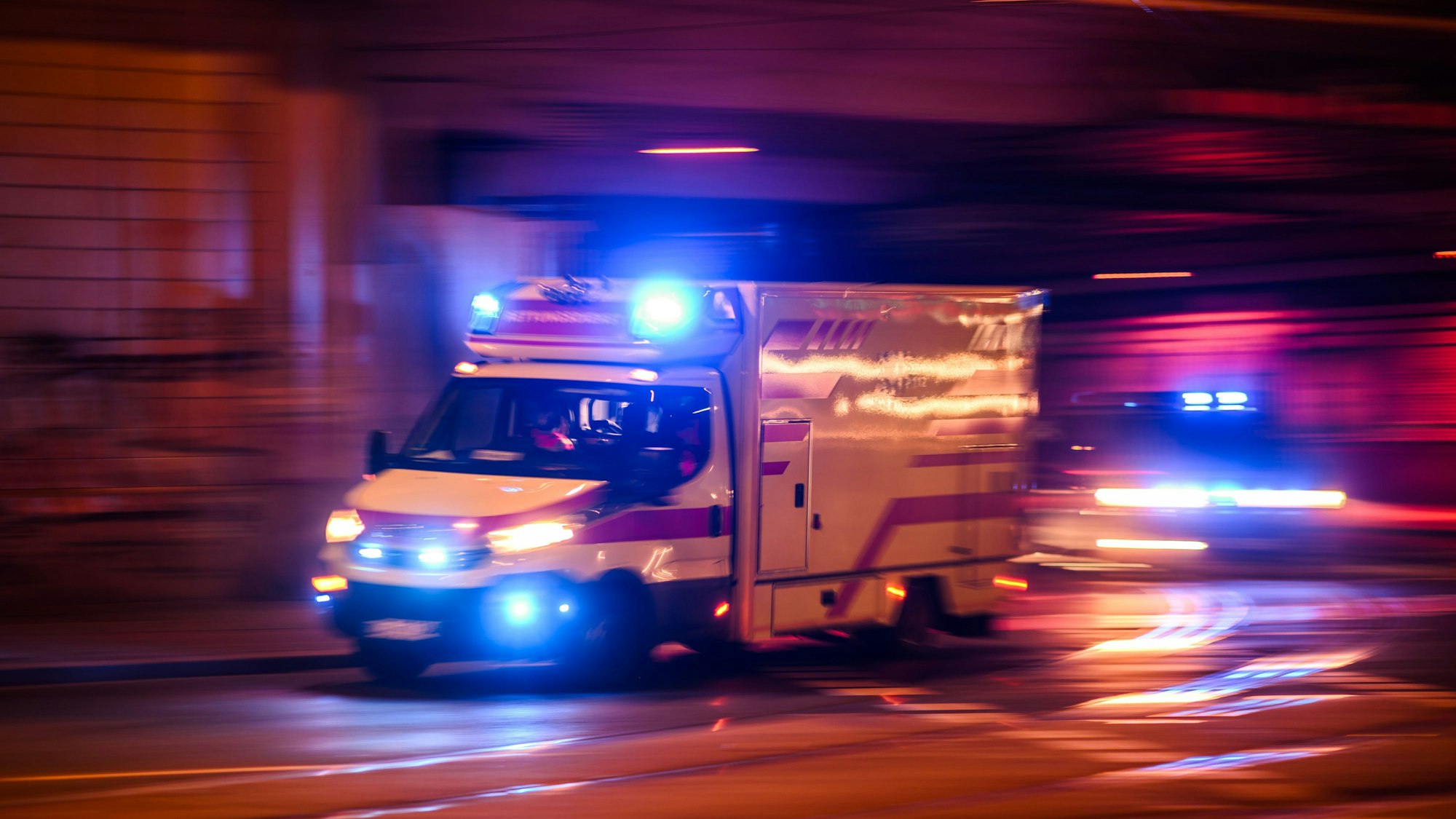 ARCHIV - 30.01.2024, Sachsen, Dresden: Ein Rettungswagen fährt am Abend auf der Antonstraße im Stadtteil Leipziger Vorstadt mit Blaulicht zu einem Einsatz, dahinter fährt ein Polizeiauto. (Aufnahme mit langer Belichtungszeit) (zu dpa: «Polizei: 13-Jährige verletzt Schwester - Siebenjährige tot») Foto: Robert Michael/dpa +++ dpa-Bildfunk +++