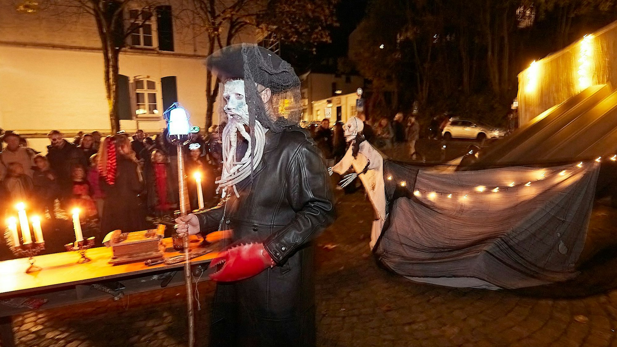 Kapitän Davy Jones, schwarz gekleidet und weiß geschminkt, schiebt einen Tisch mit Kerzen darauf durch die Straßen.