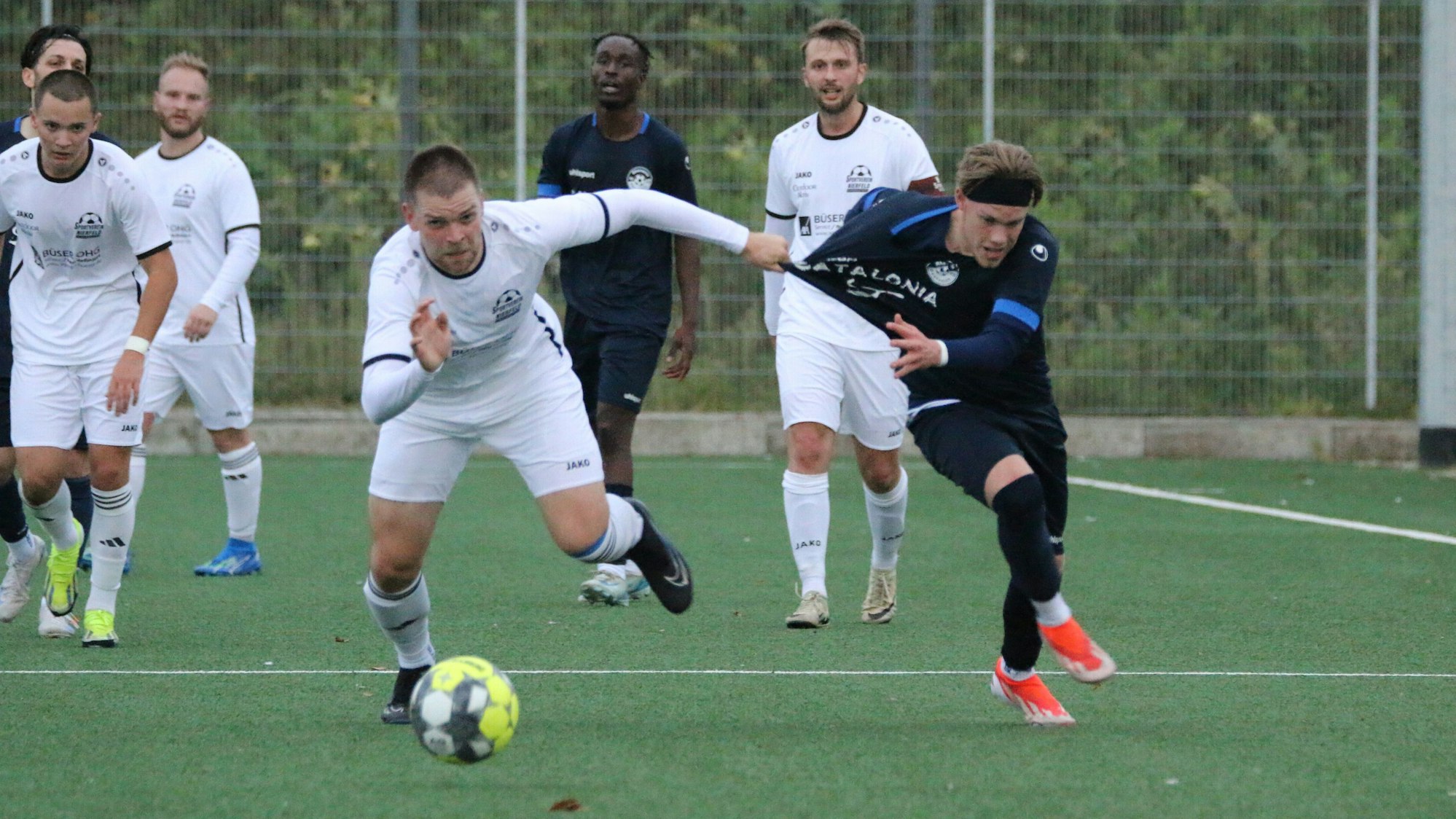 Ein Fußballspieler zieht seinem Gegenspieler beim Kampf um den Ball am Trikot.