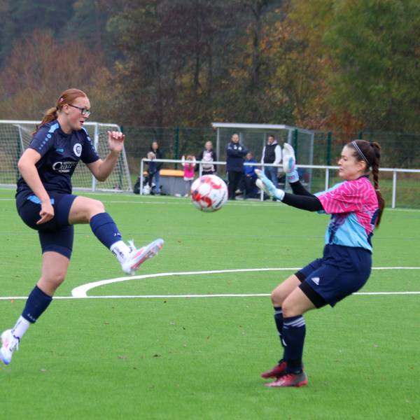 Eine Fußballerin chippt einen Ball über die herannahene Torhüterin.