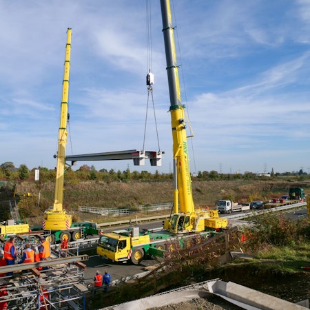 An zwei Kränen ist ein Brückenelement befestigt.