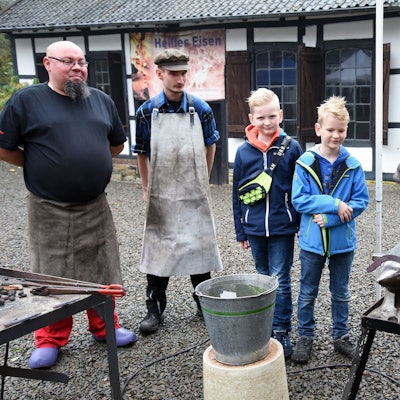Am Amboss zeigt ein Schmiedemeister, wie mit vielen Hammerschlägen ein Hufeisen entsteht.