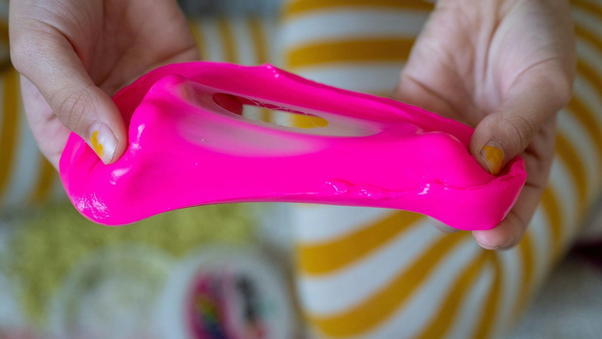 Ein Mädchen nimmt pinken Spielschleim aus einer Dose.