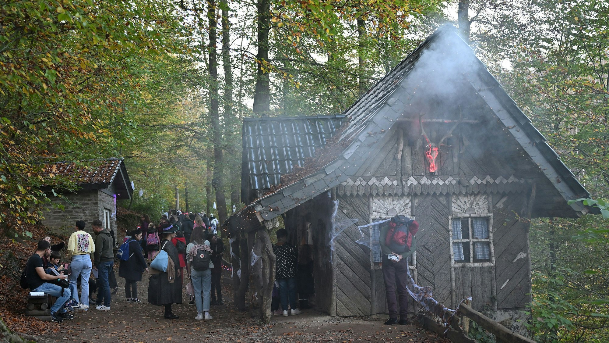 Nebel steigt an einem Haus im Altenberger Märchenwald auf, davor stehen Menschen.