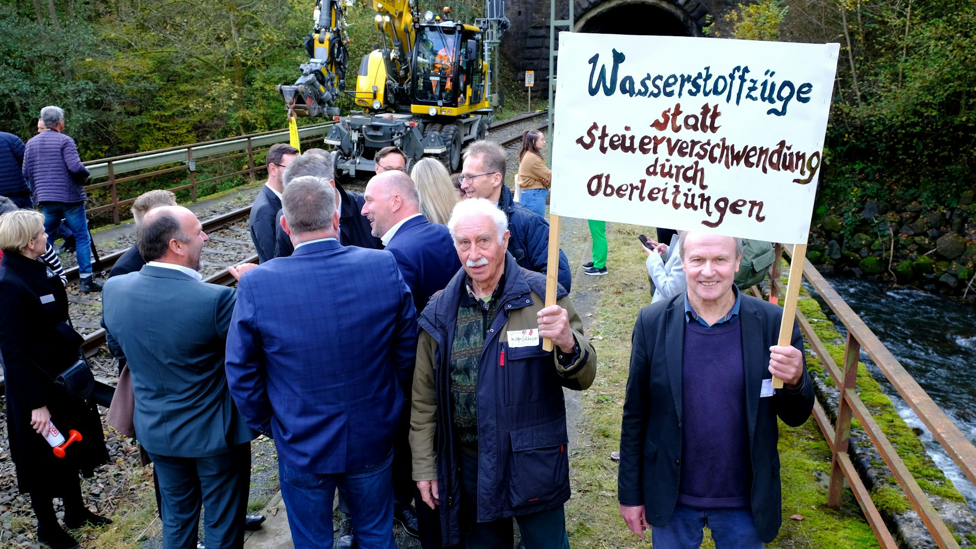 Edgar Schloesser und Peter Struben halten ein Transparent mit der Aufschrift „Wasserstoffzüge statt Steuerverschwendung durch Oberleitungen“ hoch.