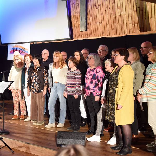 Eine Gruppe von Frauen und Männern steht auf einer Bühne und singt.