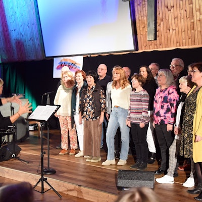 Eine Gruppe von Frauen und Männern steht auf einer Bühne und singt.