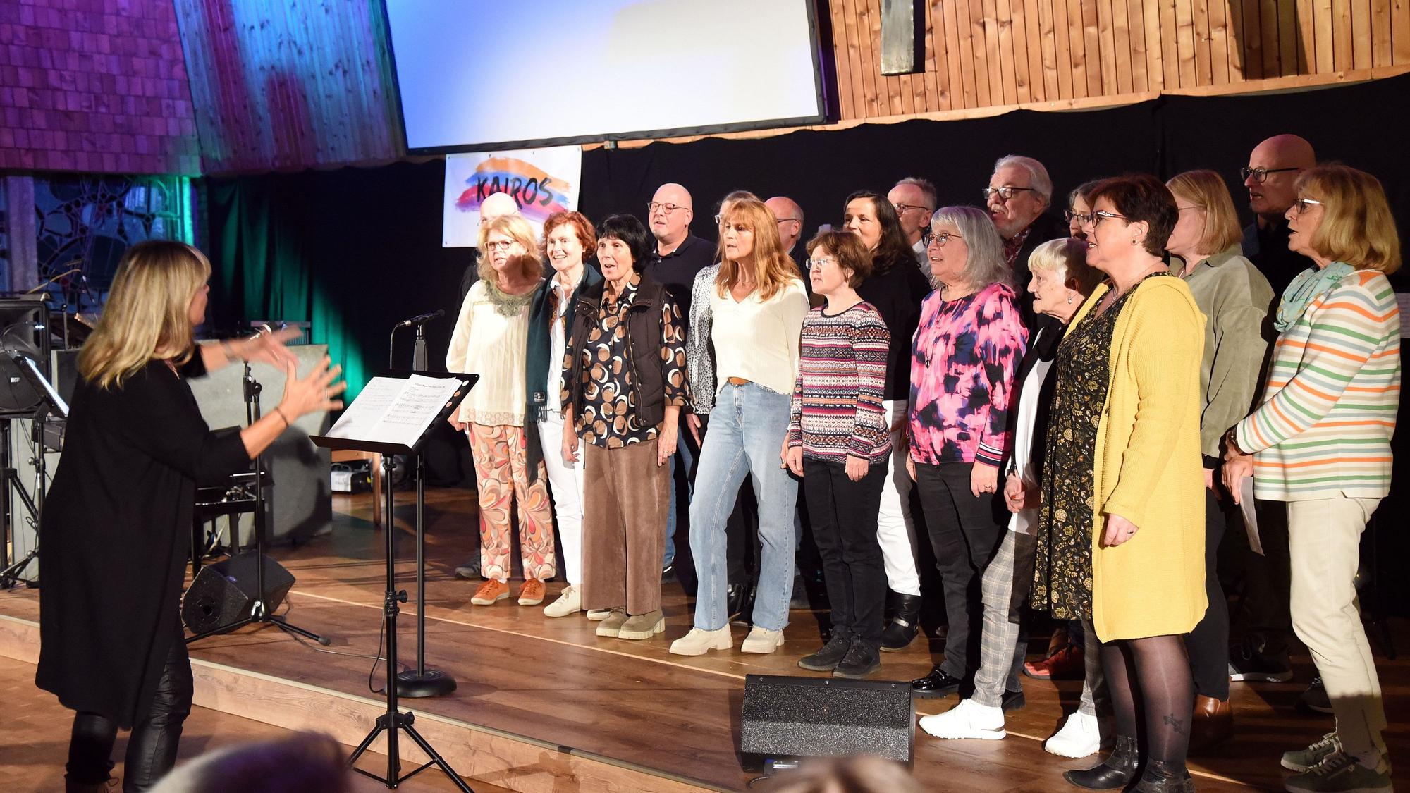 Eine Gruppe von Frauen und Männern steht auf einer Bühne und singt.