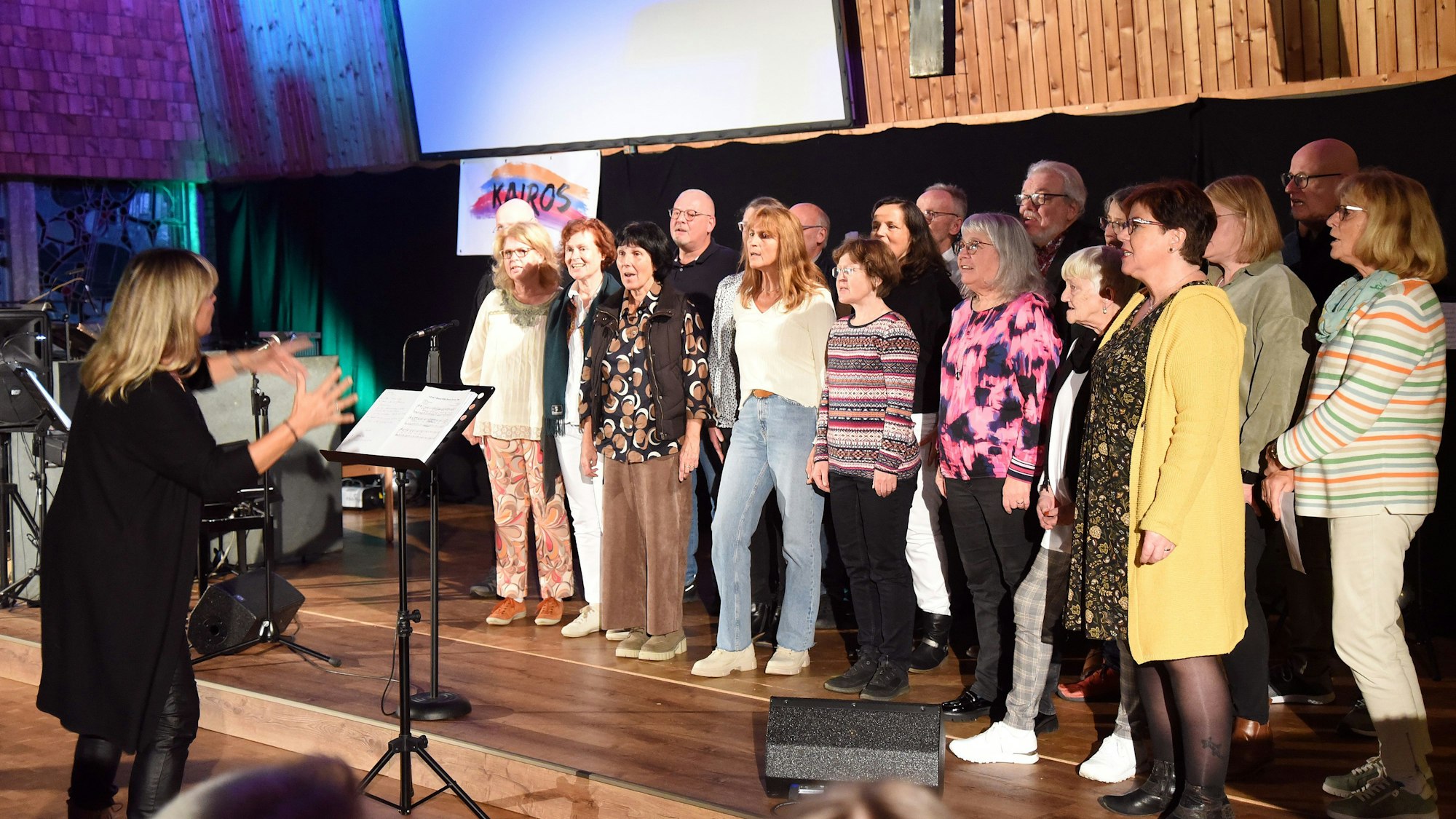 Eine Gruppe von Frauen und Männern steht auf einer Bühne und singt.