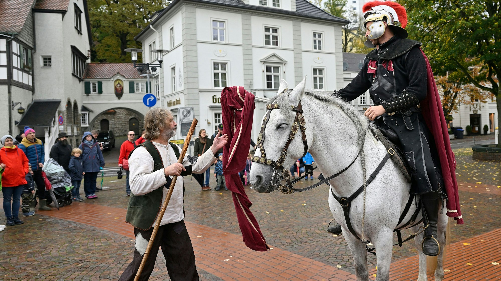Ein als St. Martin verkleideter Schauspieler teilt seinen Mantel mit einem als Bettler verkleideten Schauspieler.