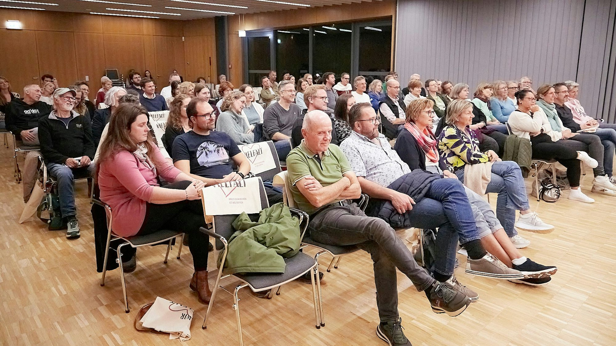 Frauen und Männer sitzen in Reihen in einem Saal.