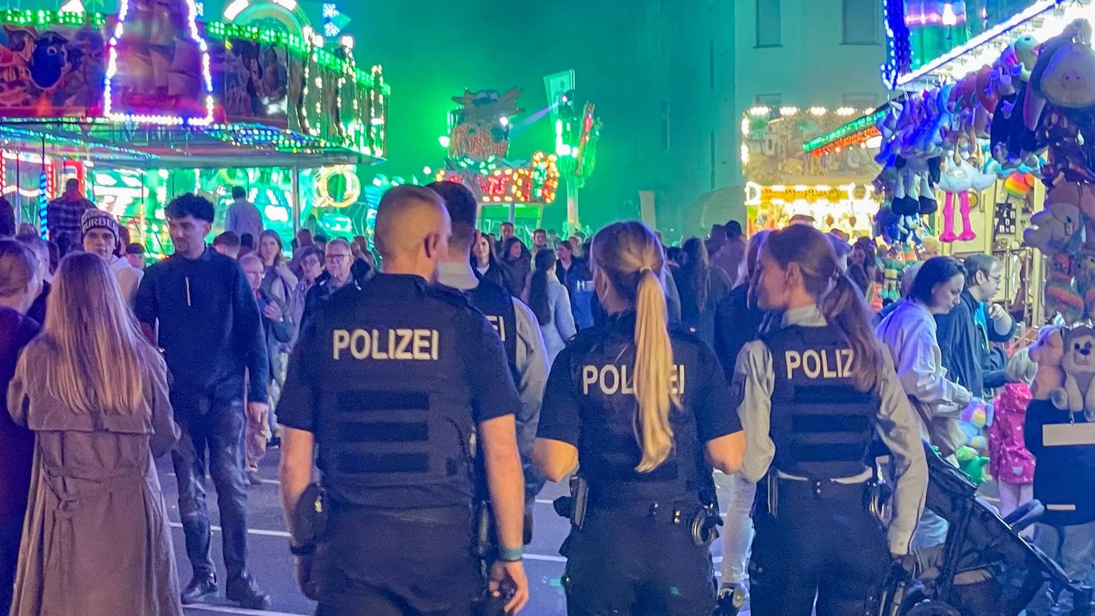 Das Bild zeigt vier Polizeibeamte, die über den Kirmesparcours gehen.