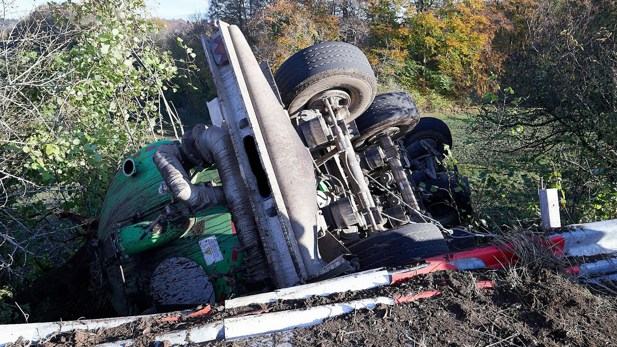 Ein Gülleanhänger liegt umgestürzt hinter einer durch den Unfall beschädigten Leitplanke.