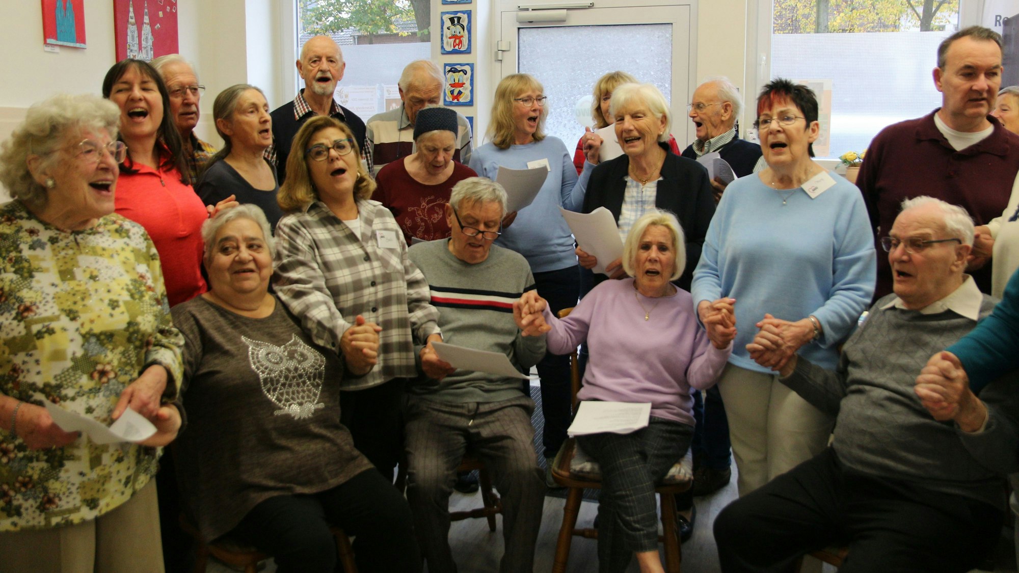 Frauen und Männer singen, einige sitzen, andere stehen. Einige halten sich an den Händen.