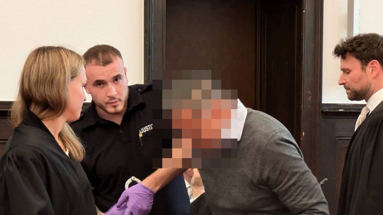 Dem ehemaligen Geschäftsführer werden von einem Justizbeamten die Handfesseln abgenommen.