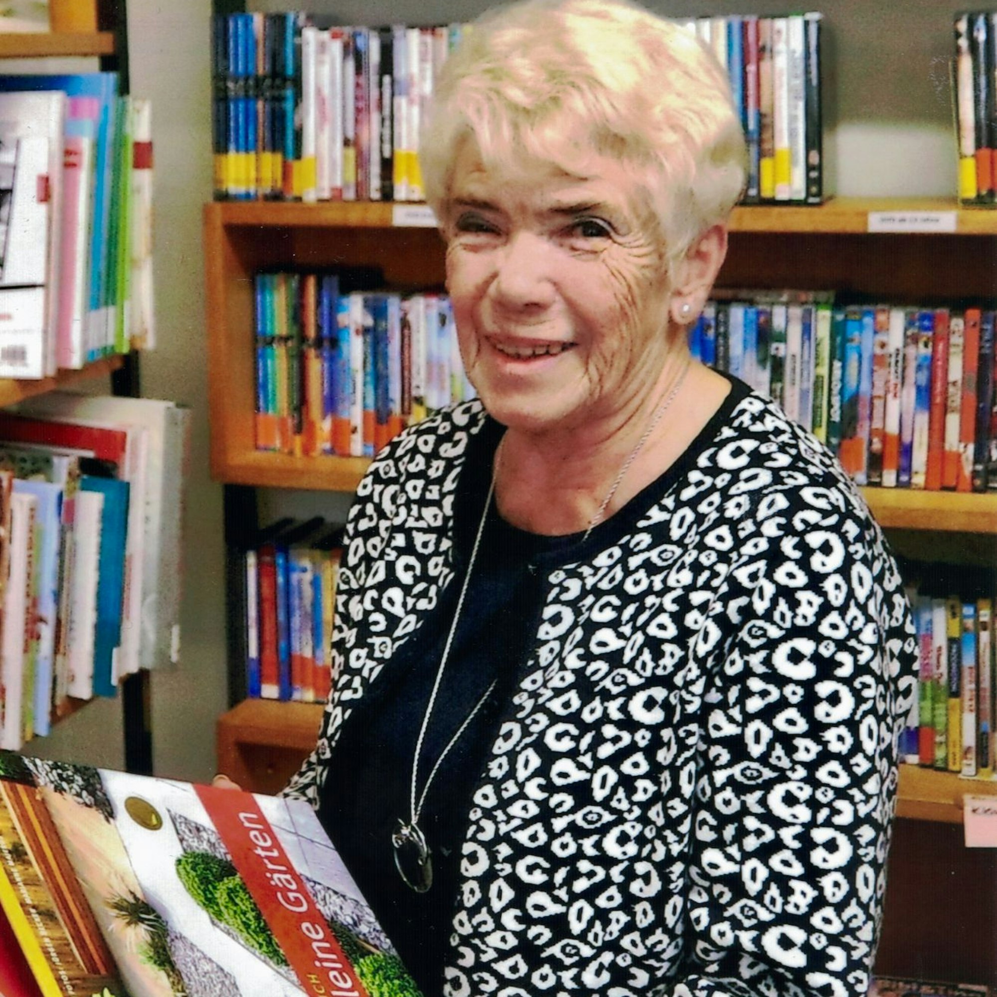Anneliese Neuber mit Büchern vor Bücherregalen einer Bibliothek.