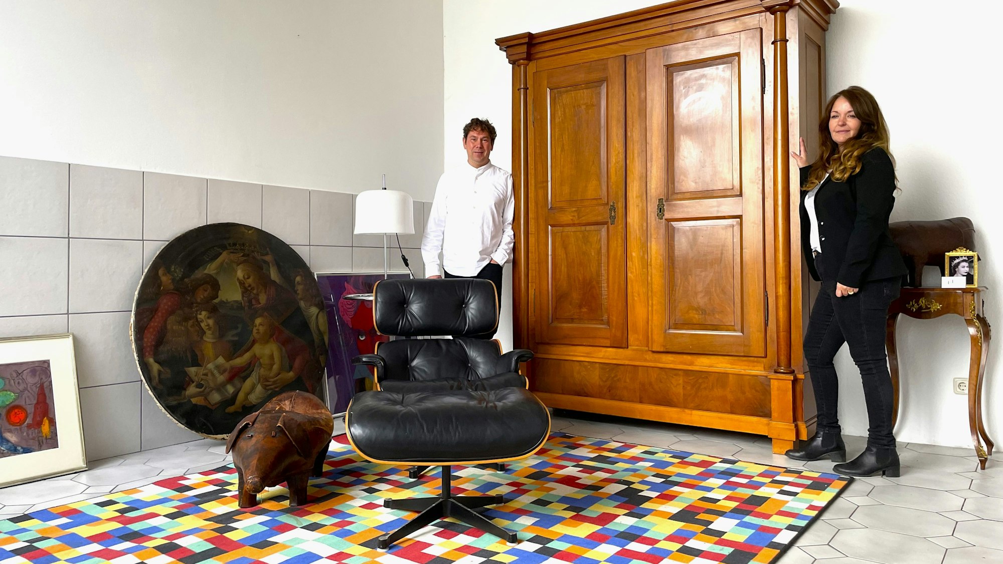 Thomas Dyck mag moderne Designerklassiker, Linda Brovot liebt antike Möbel. Beide lehnen an einem Empire Schrank von ca. 1800, im Vordregrund steht ein Eames Lounge Chair aus dem Jahre 1956, auf dem Fußboden liegt ein „1024 Farben Gerhard Richter Teppich“.