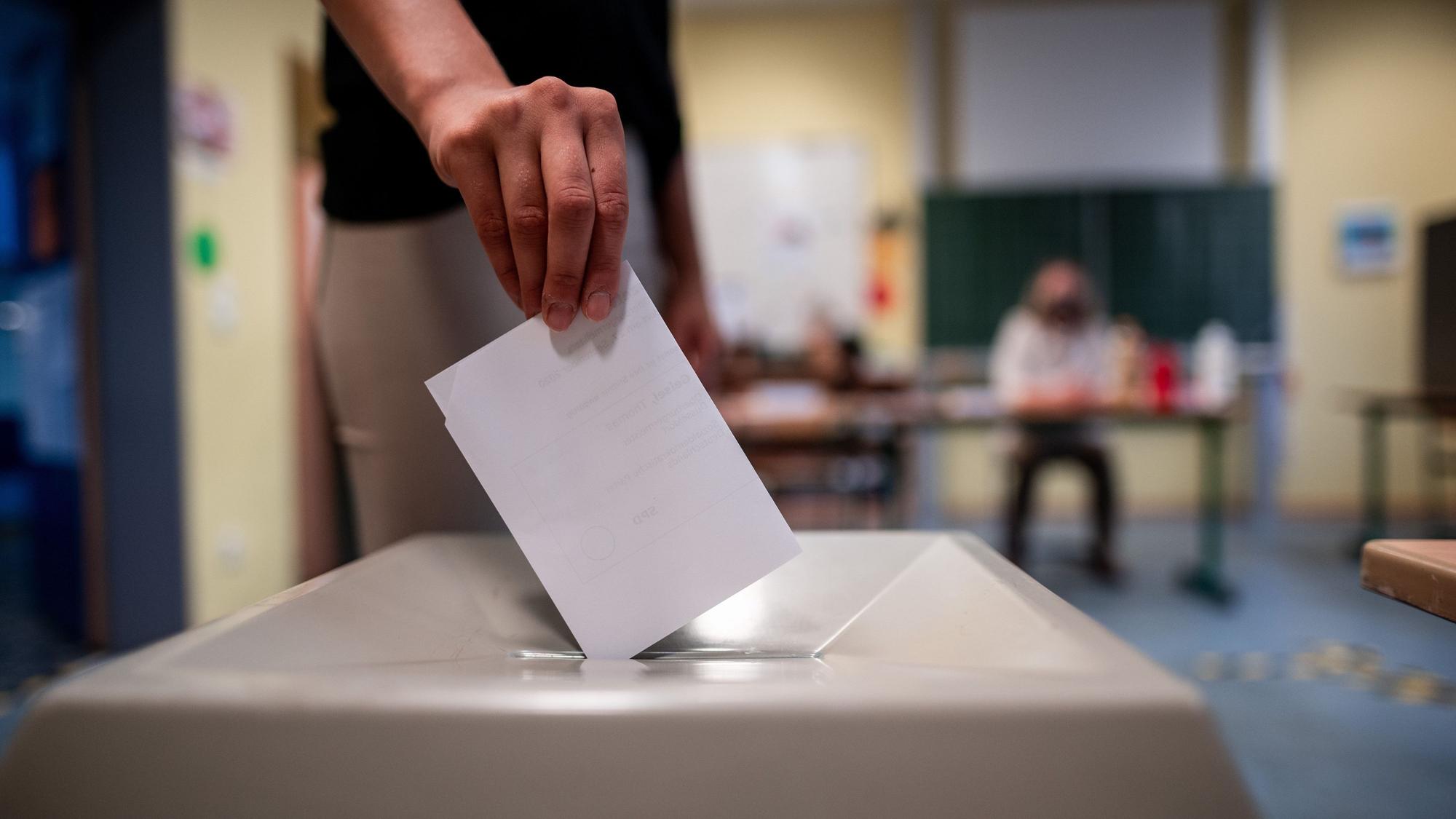 Eine Frau wirft einen Wahlschein in eine Wahlurne.
