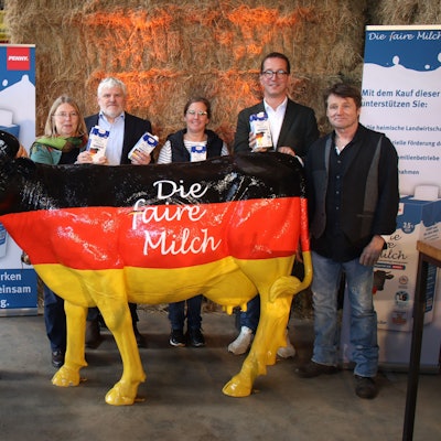 Die Vertragsunterzeichner stehen vor Strohballen und hinter einer schwarz-rot-goldenen Kuh. Einige halten Milchtüten in der Hand.