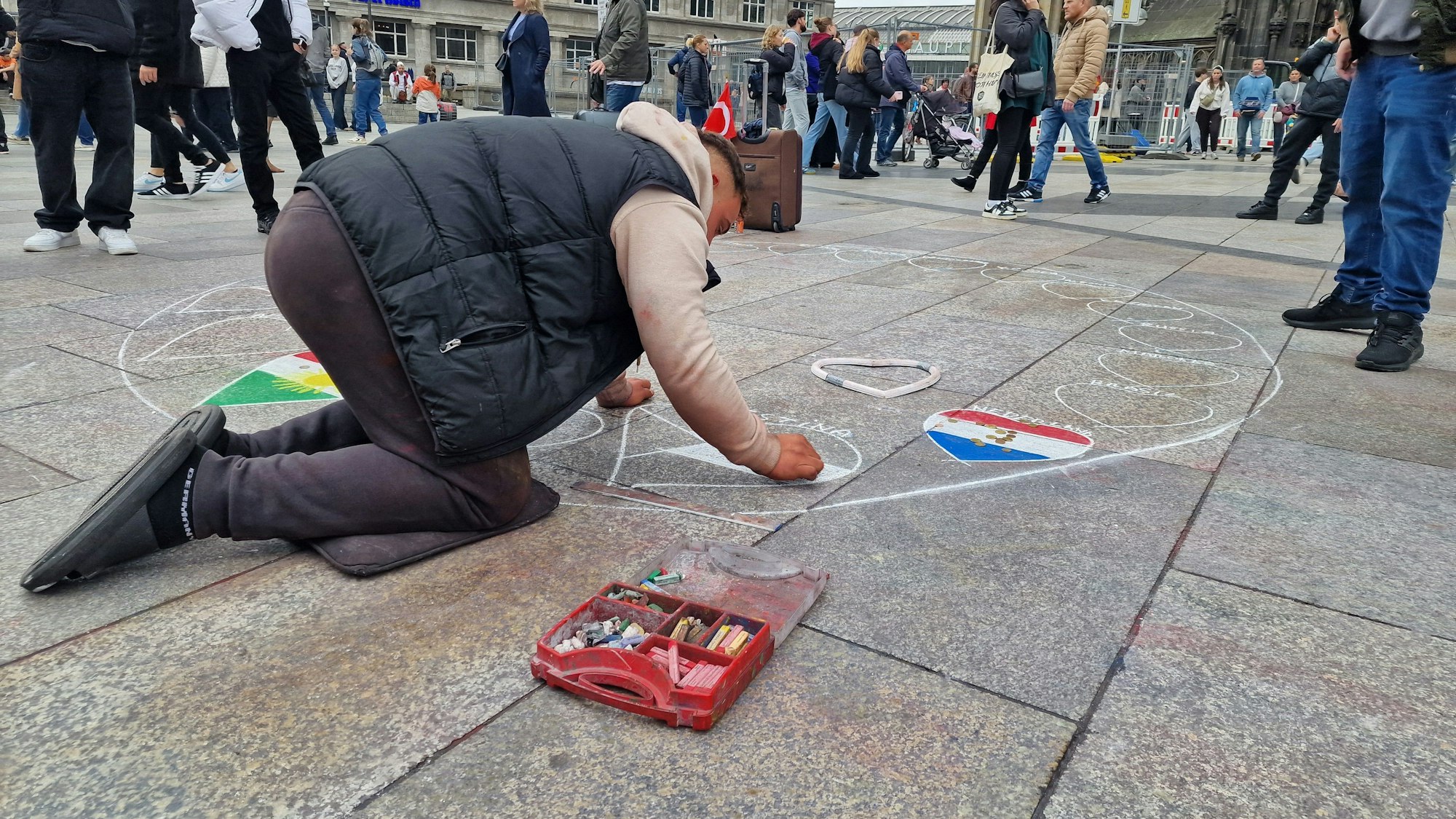 Ein Straßenmaler auf der Domplatte zeichnet mit einer Schablone Herzen auf und malt sie in der Farbe von verschiedenen Länderflaggen aus. (Archivbild)