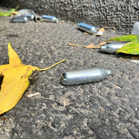 Auf einer Straße liegen mehrere Gaspatronen mit Lachgas.