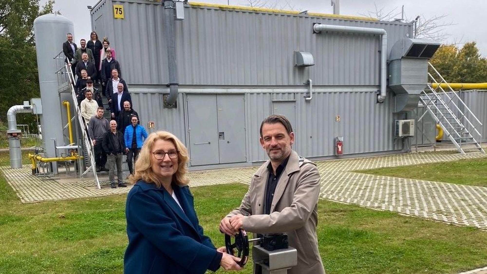 Steb-Vorständin Ulrike Franzke und Umweltdezernent William Wolfgramm nehmen die Biogasaufbereitungsanlage symbolisch in Betrieb; im Hintergrund die Projektbeteiligten auf der Treppe der Anlage.