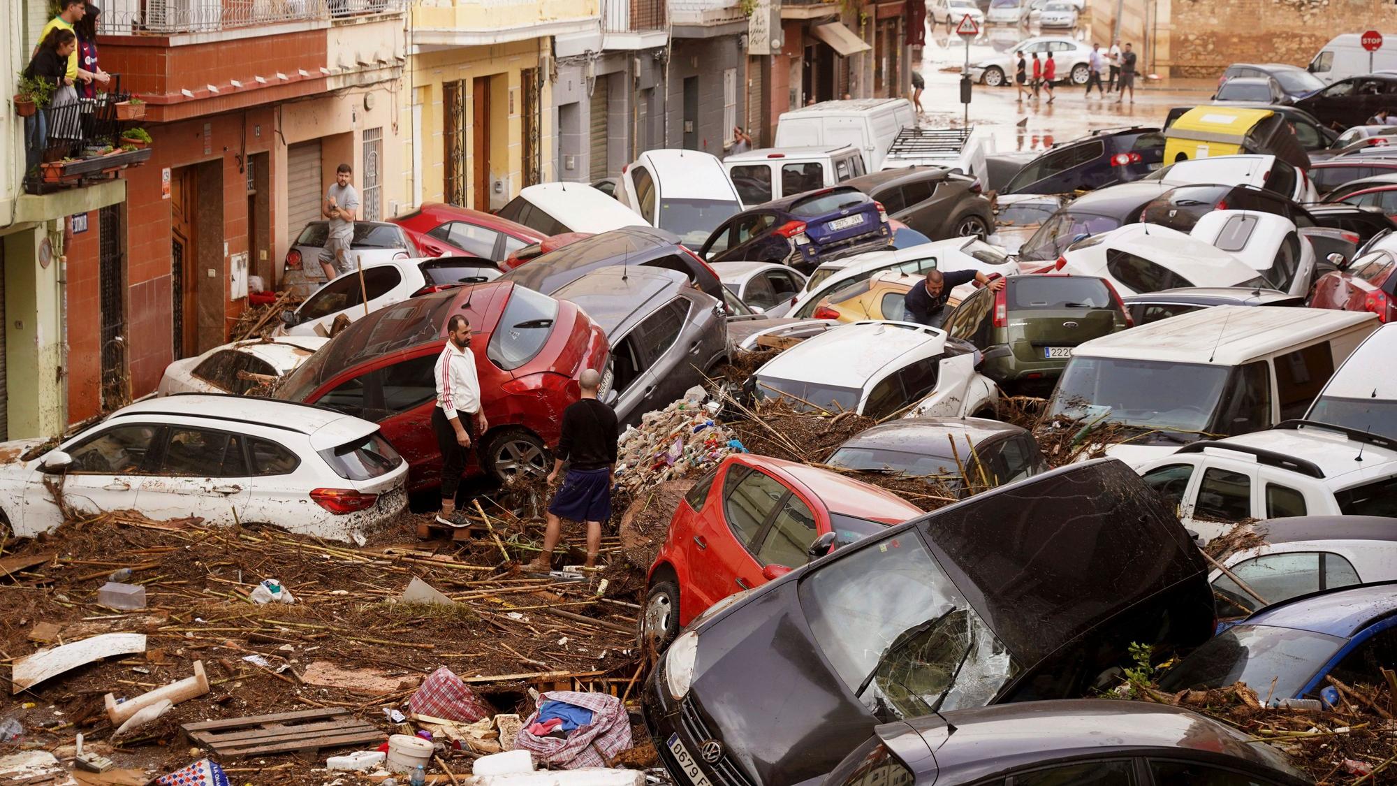 30.10.2024, Spanien, Valencia: Anwohner betrachten durch die Wassermassen aufgestapelte Autos. Foto: Alberto Saiz/AP +++ dpa-Bildfunk +++